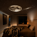 A modern bedroom with a large illuminated moon and starry sky ceiling fixture, showing a cozy bed with a black-and-white faux fur throw blanket.